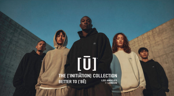 Models wearing oversized hoodies from the ['INITIĀTION] COLLECTION by ['LĒAGUE] standing together in a modern architectural setting