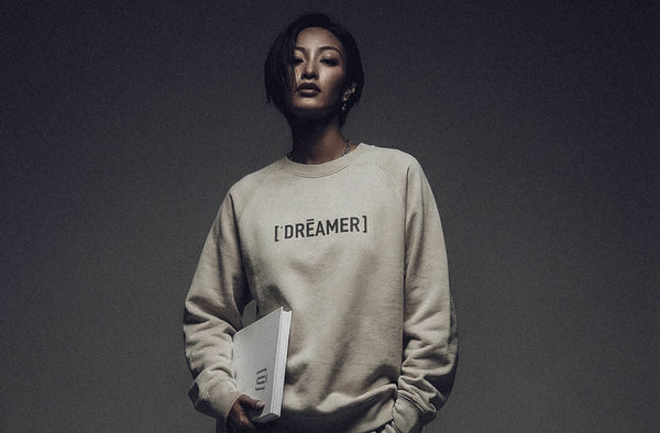 Model wearing ['DRĒAMER]™ sweatshirt in neutral tone, minimal studio lighting