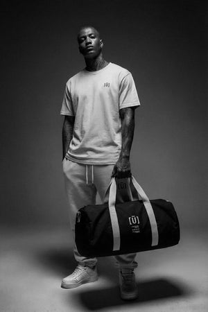 Man holding a black duffel bag with a logo on a dark background