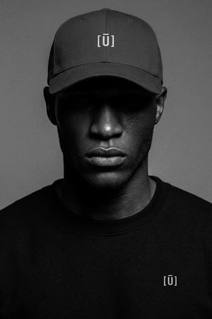 Person wearing a black cap and shirt with a logo on a gray background