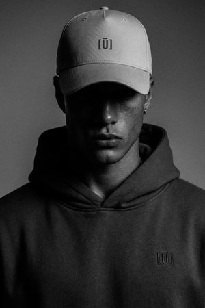 Person wearing a cap and hoodie with a logo on a dark background