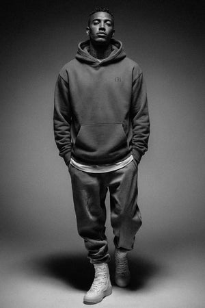 Person wearing a dark hoodie and pants on a gray background