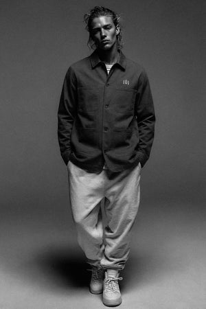 Curly haired male model wearing a structured jacket with an emblem with sweatpants and sneakers